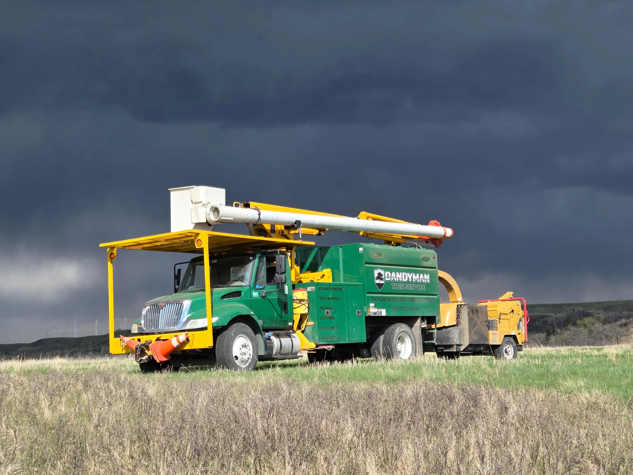 Dandyman bucket truck and chipper parked under a dark Southern Alberta sky