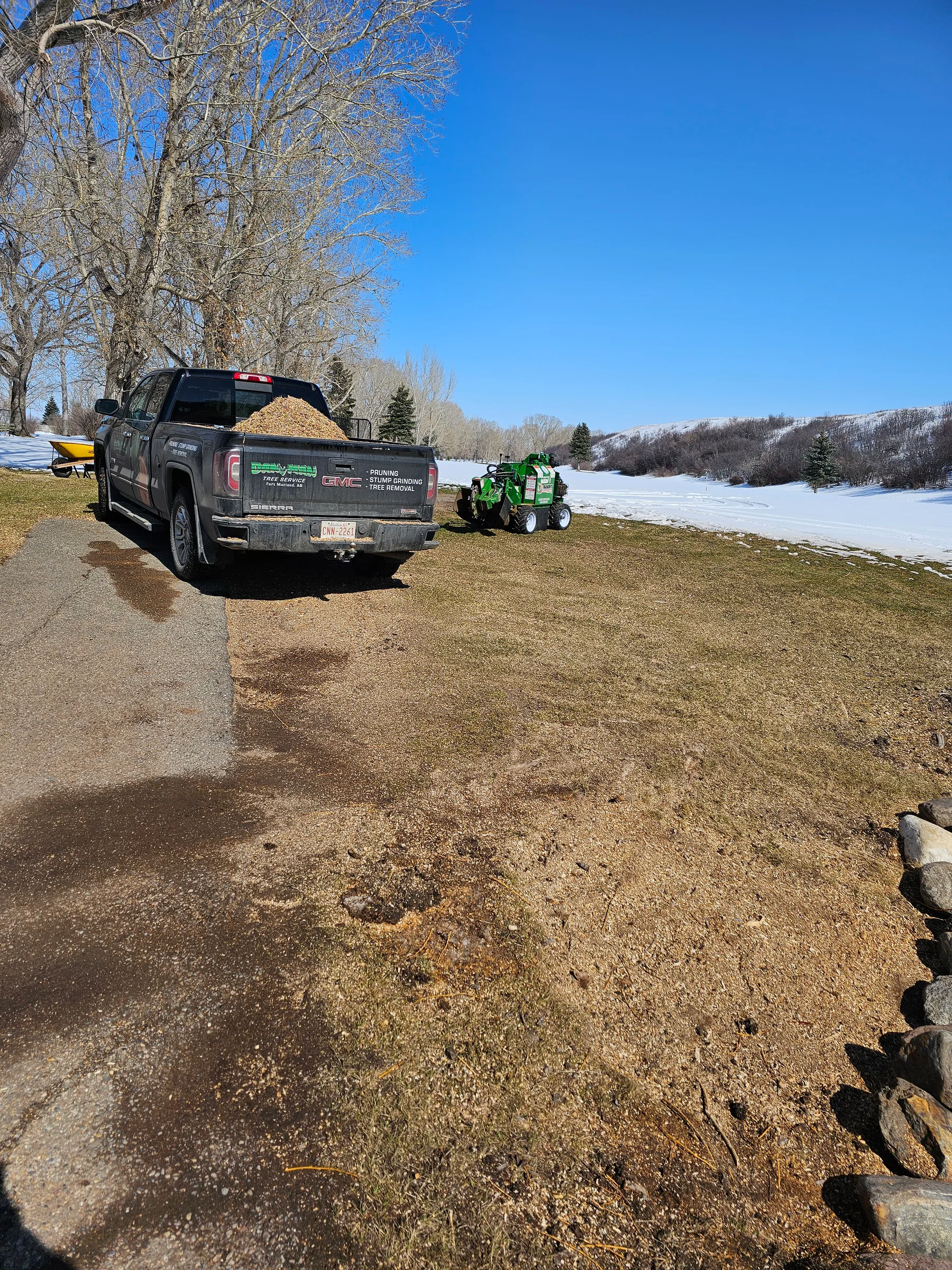 Dandyman truck and stump grinder working beside an open winter landscape
