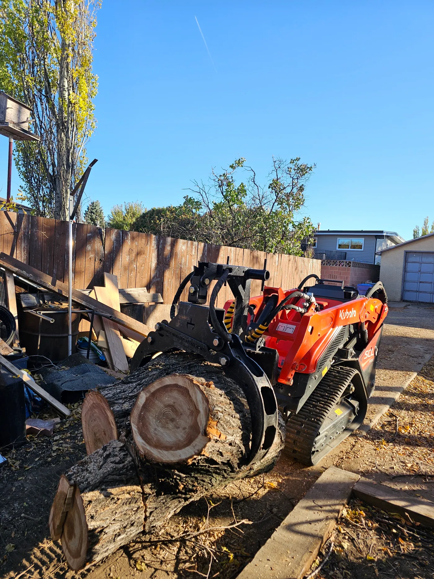 Compact loader moving heavy trunk rounds through a fenced access point